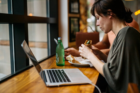Woman working from a cafe stops to eat a sandwich
