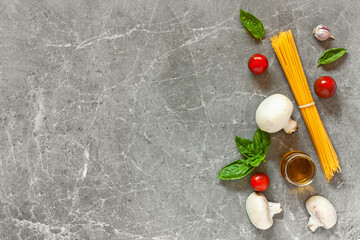Top view of ingredients for pasta with mushrooms: spaghetti, basil, garlic,cherry and olive oil on gray stone background