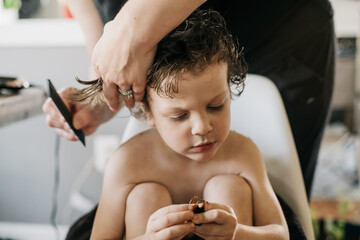 Preschool age boy having his hair cut by his mother