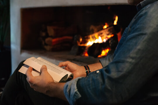 Anonymous Man Reading Book by Fireplace