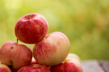 Red apples lie on a wooden board. Green blurred background. Close-up.
