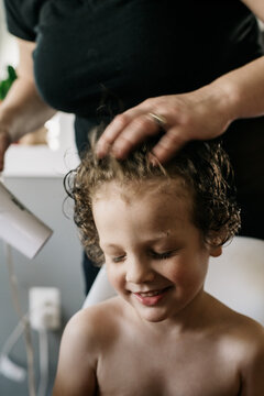 Young boy smiles while getting cut hair blown from him with a hairdryer