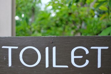 Close up an old wooden Toilet signboard on a pole in outdoor space with green garden background