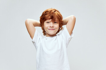 Smiling redhead boy holding hands behind his head smiling white T-shirt 