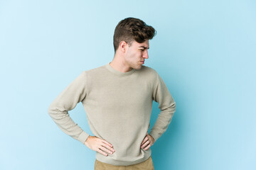 Young caucasian man isolated on blue background suffering a back pain.