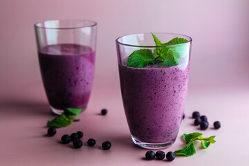 two glasses of homemade smoothie milkshake with fresh blueberries with mint leaves on pastel pink background. healthy lifestyle concept.