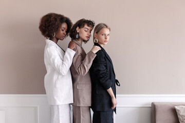 A small group of fashion multiracial multiethnic young beautiful sensual models are posing near the wall in studio room. Togetherness.