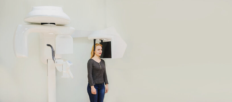 Close up portrait of young female dental patient standing in digital cephalometric panoramic x-ray machine.