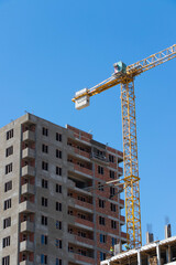 The construction crane and the building against the blue sky