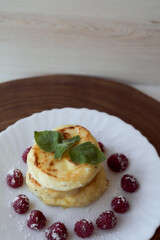Juicy curd cheesecakes lie on a white saucer with raspberries and mint leaf. Light background