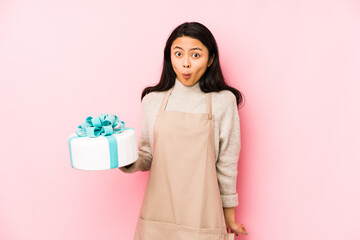 Young chinese woman holding a cake isolated points with thumb finger away, laughing and carefree.