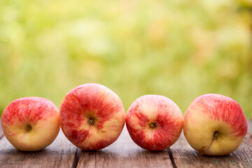 Red apples lie on a wooden board with dry spikes. Green blurred background