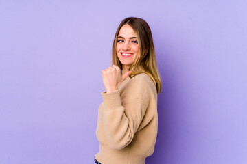 Young caucasian woman isolated on purple background points with thumb finger away, laughing and carefree.