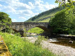 Fototapeta na wymiar The bridge over the River Wharfe, in Kettlewell, with long grasses, old trees and stones in, Kettlewell, Skipton, UK
