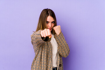 Young caucasian woman isolated on purple background throwing a punch, anger, fighting due to an argument, boxing.