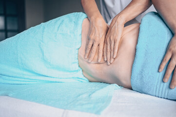 Young unrecognizable woman lying on massage table and enjoying therapeutic massage. Body care,...