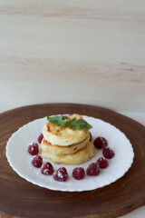Juicy curd cheesecakes lie on a white saucer with raspberries and mint leaf. Light background