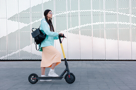 Pretty young brunette beautiful woman are riding electric scooter in summer in town