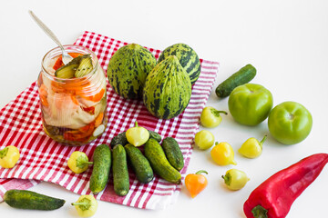 Making pickle with unripe vegetables;melon,green tomatoes,cucumber and pepper on the red fabric napkin.Pickle jar with fork near vegetables.