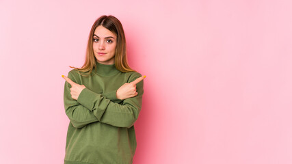 Young caucasian woman isolated on pink background points sideways, is trying to choose between two options.