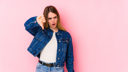 Young caucasian woman isolated on pink background showing thumb down and expressing dislike.