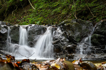Fototapeta premium Waterfall in the forest in carpathian mountains, on the background of autumn leaves. Selective focus. 