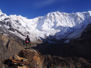 A mountain climber standing in front of a snow-covered Himalayas in the blue skies, ABC (Annapurna Base Camp) Trek, Annapurna, Nepal