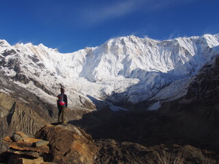 A mountain climber standing in front of a snow-covered Himalayas in the blue skies, ABC (Annapurna Base Camp) Trek, Annapurna, Nepal