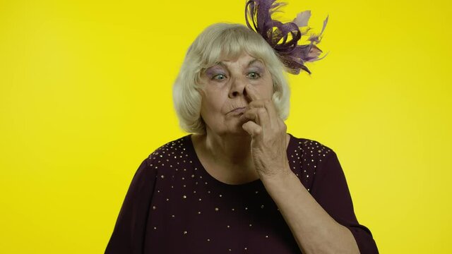Funny stupid senior old woman picking nose with silly expression, removing boogers, bad manners