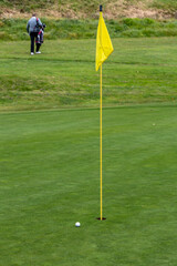 Obraz premium Golf ball lying very close to the hole on a green. A person is visible in the background.