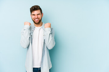 Young caucasian man isolated on blue background cheering carefree and excited. Victory concept.