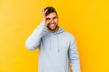 Young caucasian man isolated on yellow background excited keeping ok gesture on eye.