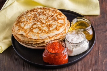 Pancakes on black plate. Fillings-sour cream, red caviar, honey. Pancake day. Russian tradition in the last week before Easter, there are pancakes with different fillings.