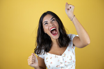 Beautiful woman over yellow background very happy and excited making winner gesture with raised...