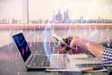 Double exposure of man's hands holding and using a digital device and forex graph drawing. Financial market concept.