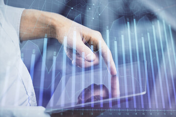 Double exposure of man's hands holding and using a digital device and forex graph drawing. Financial market concept.