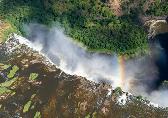 Aerial view of Victoria Falls. Water stream flowing down a canyon with a rainbow. Zambezi River in...
