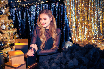 Young beautiful woman in elegant evening dress sitting on floor near christmas tree and presents on a new year eve. Interior with christmas decorations. Shallow DOF and bokeh background.