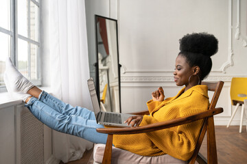 Happy African American woman freelancer with afro hairstyle wear yellow cardigan resting, sitting...