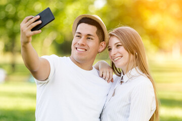Young couple taking a selfie on their mobile in the park. Latin man and Caucasian woman
