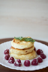 Juicy curd cheesecakes lie on a white saucer with raspberries and mint leaf. Light background