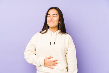 Young woman isolated on a purple background touches tummy, smiles gently, eating and satisfaction concept.