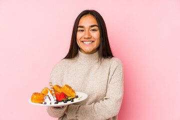 Young asian woman holding a waffle isolated laughing and having fun.