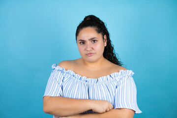 Young beautiful woman with curly hair over isolated blue background skeptic and nervous,...