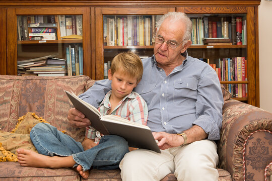 Grandfather and grandson reading a book on a sofa together