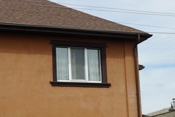 one large window on a brown wall of a private house under a tiled roof against the sky