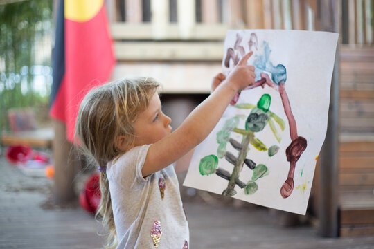 Preschool child holds up her painting to look at
