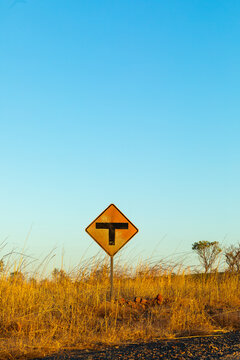 T-junction sign in long dry grass with blue sky above