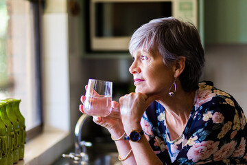 Portrait of a healthy senior woman leaning on the kitchen bench drinking a glass of water