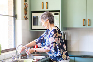 senior woman filling water jug from tap in kitchen